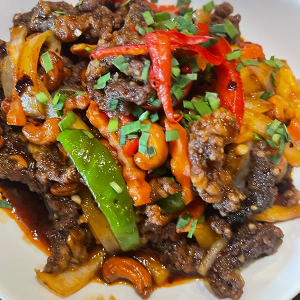 Close-up of a beef stir-fry with colorful peppers, cashews, and green onions on a white plate.