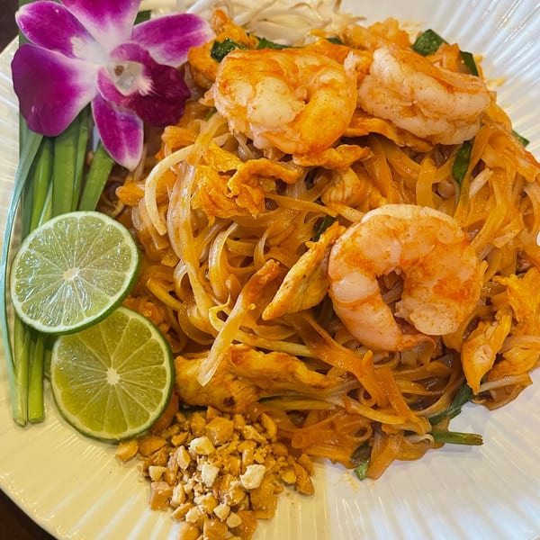 Pad Thai with shrimp, chicken, lime, peanuts, and a purple orchid on a white plate.
