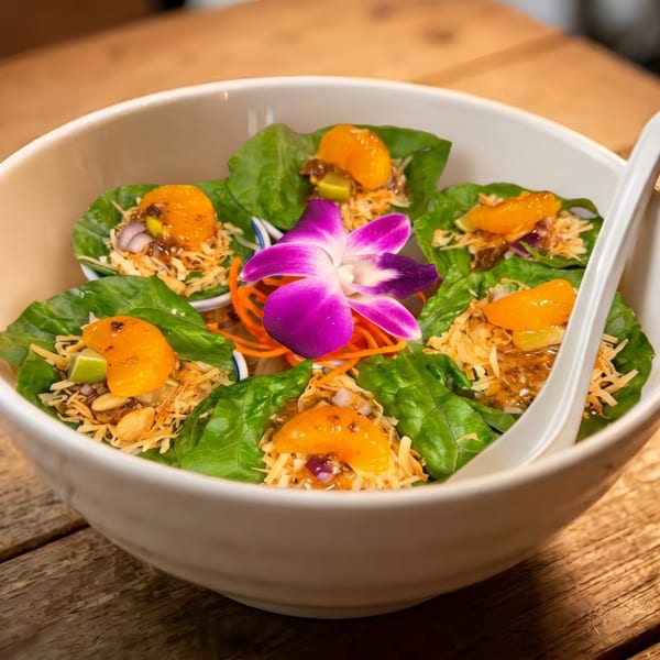 A white bowl filled with green lettuce wraps, topped with orange slices, nuts, and sauce.